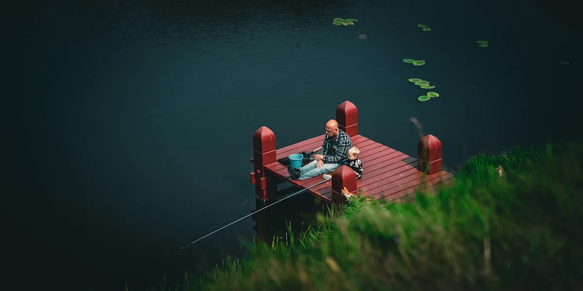 Father and child fishing together from a wooden dock on a peaceful lake