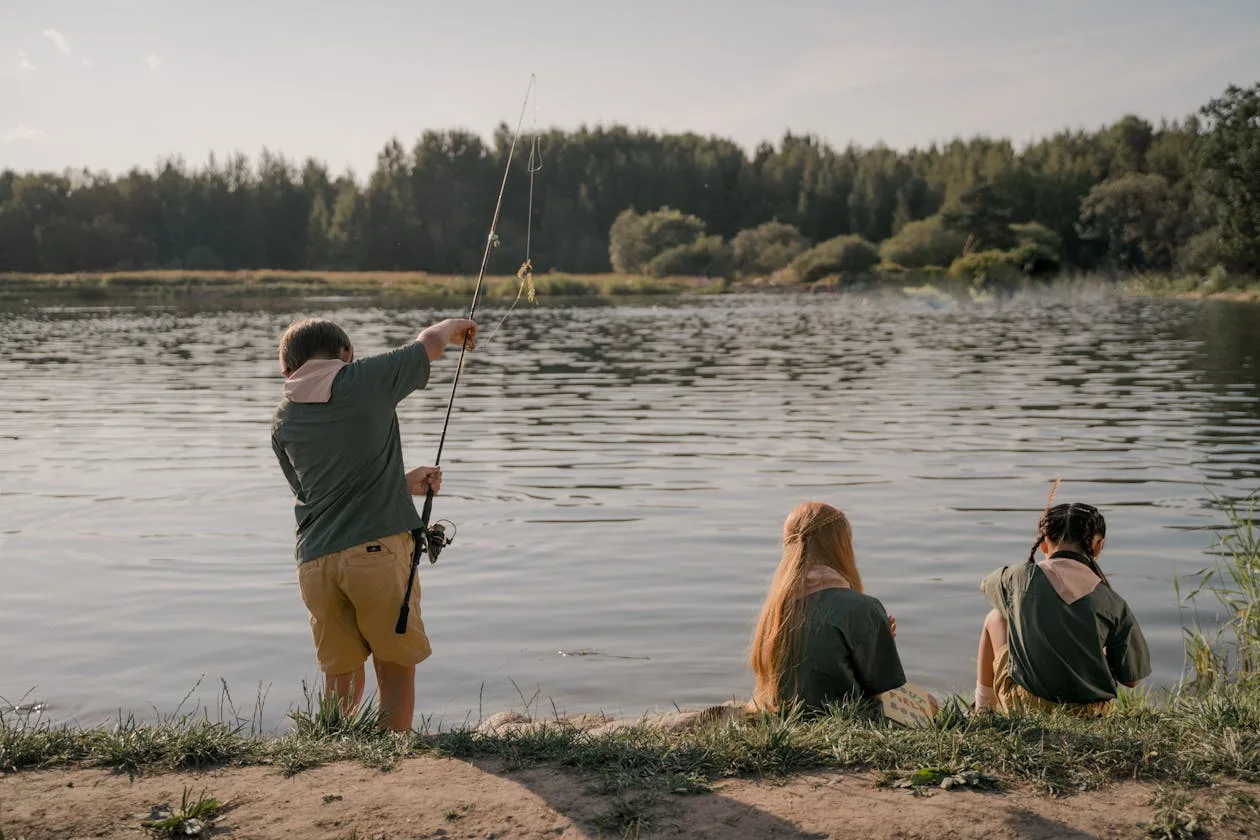 Three children fishing from the shore of a peaceful lake